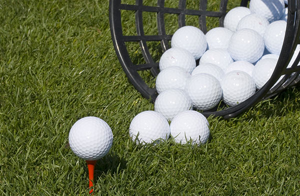 Bucket of golf balls with one golf ball on tee 